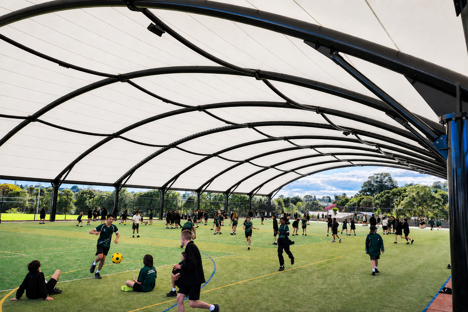 Students playing soccer under a large curved Tensara shade canopy